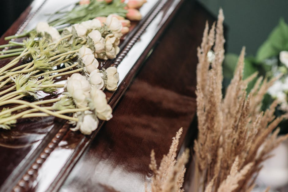 A close-up view of a floral arrangement placed on a polished wooden surface, featuring a variety of flowers in soft, neutral tones. The bouquet includes white roses, with their delicate petals and gre