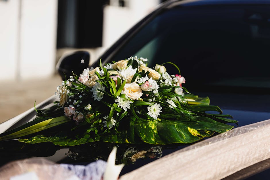 A freshly crafted floral arrangement featuring pale cream roses, white daisies, small pink and white blossoms, and green foliage, arranged as a wedding bouquet. The bouquet is placed on the hood of a 