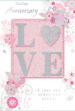 The photograph shows a romantic anniversary card whose design blends soft pastel pinks, pearly whites and silvery greys into a gentle celebration of enduring love, much like a carefully arranged bouquet delivered in Enfield Wash. At the centre, the word LOVE appears in raised, glittering letters, each stroke softly rounded and dusted with fine, shimmering particles. The letterforms are primarily blush pink with pearlescent highlights, and the glitter edges sparkle with subtle silver tones, giving the impression of light catching the edges of fresh petals. The O is delicately styled to echo the shape of a heart, adding a tender focal point without overwhelming the rest of the design. Around this central word, clusters of delicate blossoms in blush, mauve and pale ivory unfold with a watercolour softness, their outlines drawn in fine, flowing lines that curve like stems in a hand-arranged bouquet. Slender vines and swirling flourishes link each flower, while tiny accents-suggestions of petals, small curls and almost-hidden butterflies-add a feeling of motion, as if the design were gently breathing. The background is a soft pink wash, evenly toned and calming, allowing the silver detailing to glimmer quietly rather than shout. Inscribed in graceful script are the words On Our Anniversary and I love you today and always, completing the composition with genuine warmth. The card feels like a keepsake that a couple in Enfield Wash might treasure on their mantel, its design echoing the softness and sincerity of an anniversary arrangement chosen with care.